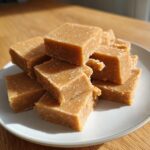 A pile of rich, square-cut peanut butter fudge recipe pieces stacked on a white plate.