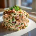 A perfectly molded portion of creamy salmon salad mixed with red onion and herbs, garnished with fresh dill.