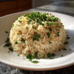 A mound of fluffy, golden rice pilaf served on a white plate and generously garnished with fresh chopped parsley.