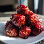 A close-up stack of shiny, glazed cranberry meatballs piled high on a white plate.