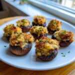 A plate of seven golden-brown stuffed mushrooms with a crunchy breadcrumb topping, garnished with parsley.