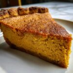 A close-up, vibrant slice of homemade sweet potato pie showing a rich orange filling and browned crust.