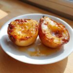 Two caramelized halves of baked pears glistening with syrup on a white plate.