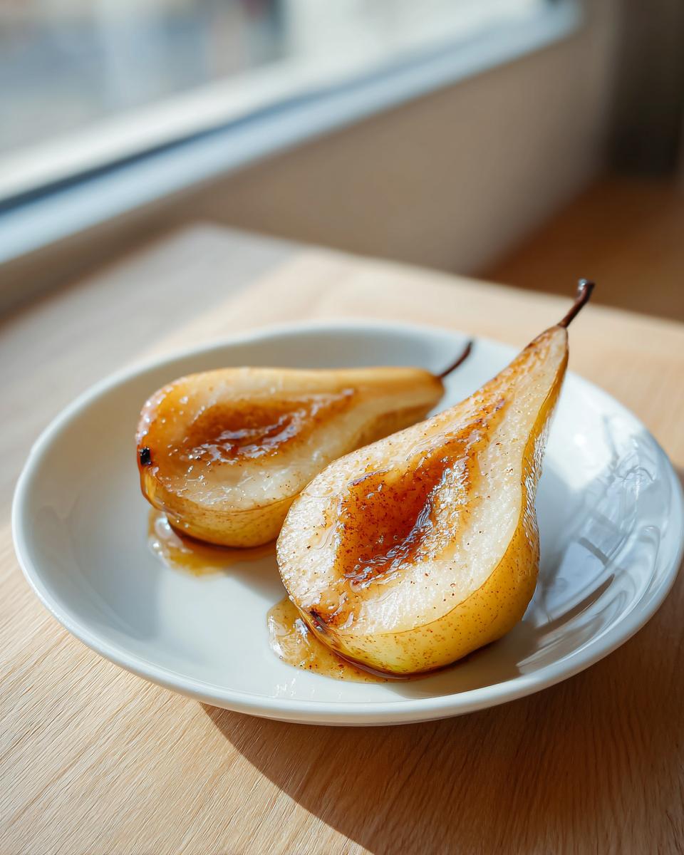 Two halves of glistening baked pears drizzled with cinnamon syrup served on a white plate.