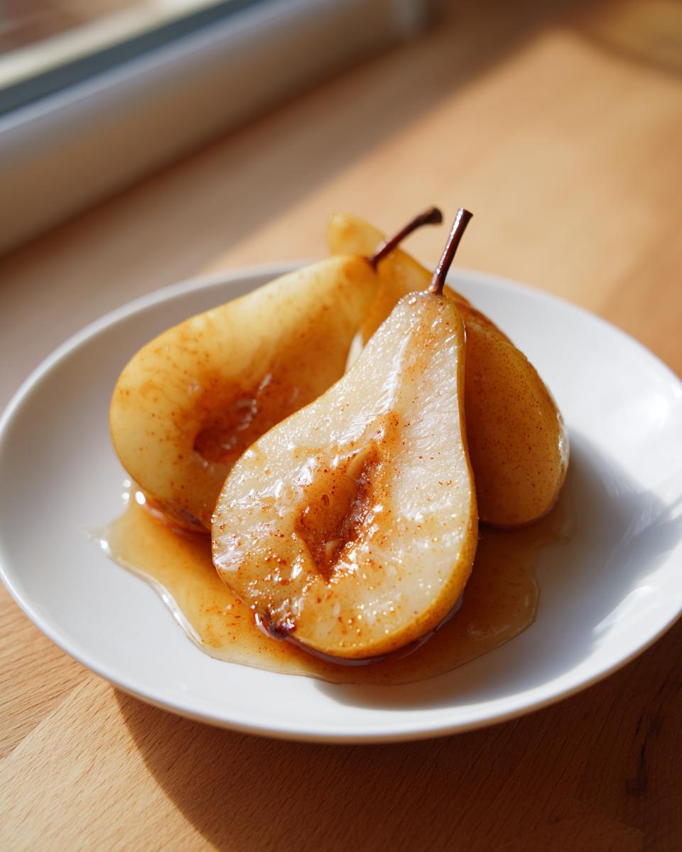 Three halves of glistening baked pears, spiced with cinnamon, sitting in sweet syrup on a white plate.
