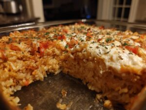 A close-up view of a freshly baked sushi bake in a metal pan, showing a thick layer of rice and creamy topping.