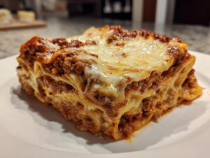 A thick, layered slice of homemade lasagna with rich meat sauce and melted cheese topping on a white plate.