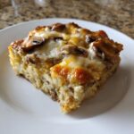 A square slice of baked breakfast casserole with cream of mushroom, topped with melted cheese and mushrooms.