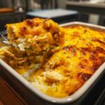 A spoonful of creamy cheesy chicken and rice lifted from a baking dish showing melted, browned cheese.