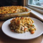 A scoop of creamy chicken and wild rice casserole topped with golden breadcrumbs on a white plate.