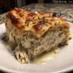 A close-up of a rich slice of chicken lasagna with creamy white sauce and a browned, cheesy top.
