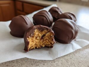 Close-up of chocolate covered pecan pie balls, one bitten to show the textured, nutty filling inside.