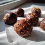 A close-up of homemade pecan pie balls dipped in rich chocolate and topped with chopped nuts.