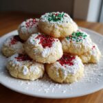 A stack of soft Christmas gooey butter cookies dusted with powdered sugar and topped with red and green sprinkles.