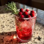 A bright red cranberry pomegranate margarita garnished with fresh cranberries and a sprig of rosemary.