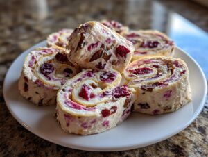 Close-up of several slices of cranberry tortilla roll ups filled with cream cheese, dried cranberries, and pecans, served on a white plate.