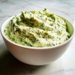 Close-up of a thick, creamy dill dip loaded with fresh green dill, served in a white bowl.