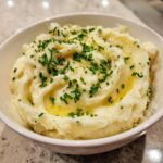 A close-up of creamy garlic mashed potatoes topped with melted butter and fresh chopped chives.