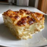 A thick, square slice of golden-brown potatoes au gratin with creamy layers on a white plate.