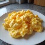 A close-up of soft, creamy, and bright yellow scrambled eggs piled high on a white plate.