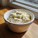 Close-up of a creamy tuna dip topped with chopped green celery, served in a small white bowl.