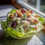 Close-up of a creamy Waldorf salad mixture, featuring grapes and walnuts, served inside a crisp lettuce cup.