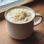 A creamy mug of white hot chocolate topped generously with white chocolate shavings.