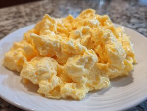 Close-up of perfectly cooked, creamy, and fluffy scrambled eggs piled high on a white plate.