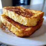 Close-up of two thick slices of fluffy easy french toast dusted heavily with cinnamon on a white plate.