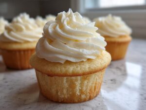 Close-up of a perfectly baked vanilla cupcake topped with a tall swirl of white vanilla buttercream frosting.