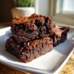 Close-up of two fudgy sweet potato brownies stacked on a white plate, showing chocolate chips.