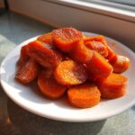 A mound of bright orange, thickly sliced glazed carrots glistening with syrup on a white plate.