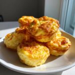 A stack of fluffy, golden brown baked egg bites piled high on a white plate, perfect for a quick breakfast.