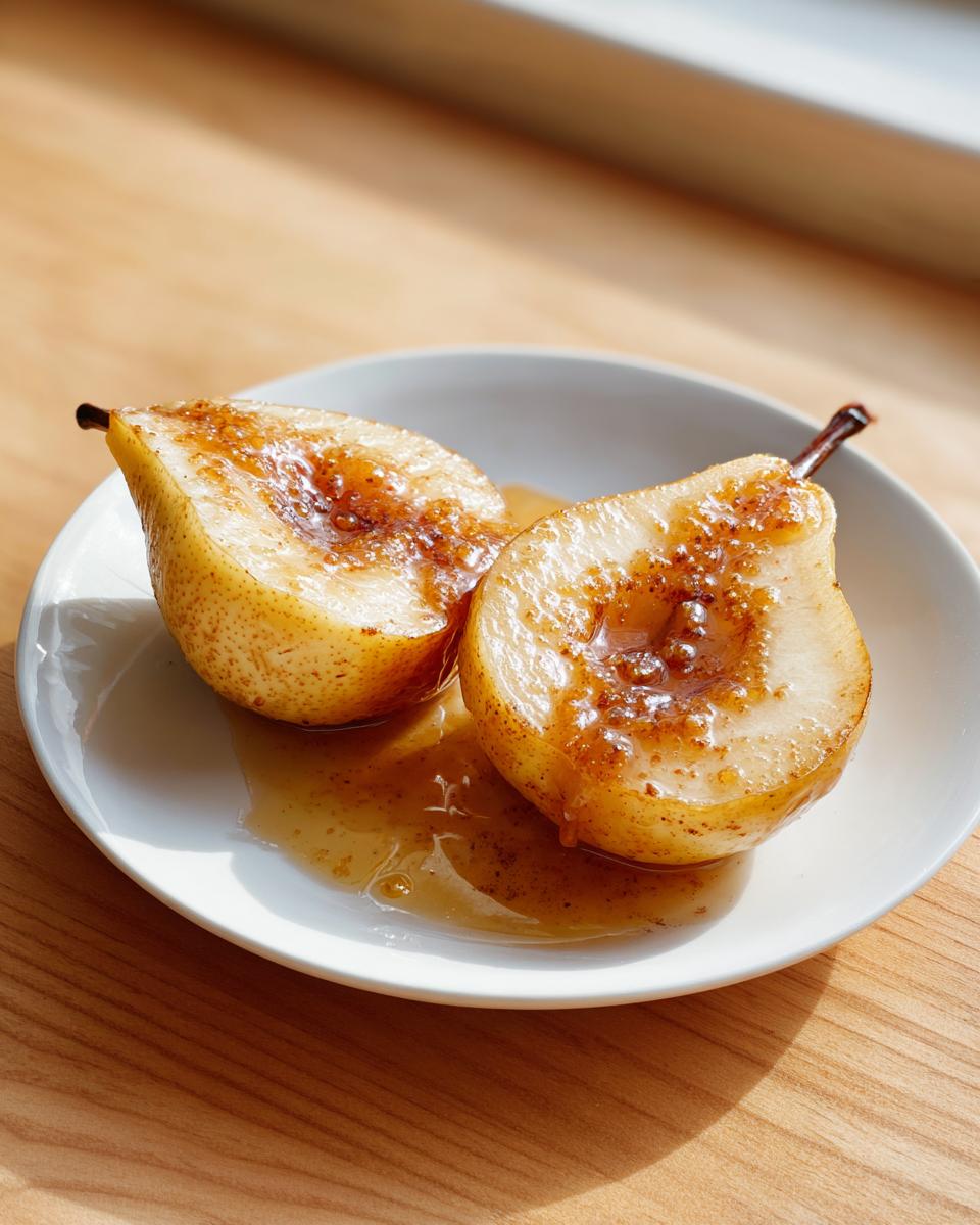 Two halves of glistening baked pears served on a white plate with sweet syrup.