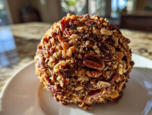 A close-up of a perfectly formed Holiday cheese ball completely coated in chopped and whole pecans.