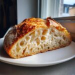 A close-up of a thick slice of Italian bread showing an airy, open crumb structure and a dark, crispy crust.