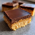 A close-up of a square lunch lady peanut butter bars slice showing a crumbly base, thick caramel layer, and smooth chocolate topping.