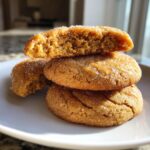 A stack of three soft maple brown sugar cookies, one broken open to show the chewy interior and drizzled with glaze.