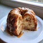 A slice cut from a small bundt-style apple cake, generously topped with a thick caramel glaze.