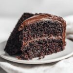 Two rich, dark slices of moist chocolate fudge cake topped with thick chocolate frosting on a white plate.