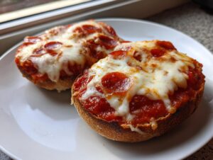 Close-up of two halves of a pepperoni english muffin pizza with melted mozzarella cheese on a white plate.