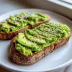 Two slices of delicious avocado toast topped with mashed and sliced avocado and everything bagel seasoning.