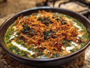 A rich bowl of Persian noodle soup topped with crispy fried onions, dried herbs, and a swirl of yogurt or kashk.