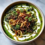 Top-down view of a vibrant Persian noodle soup topped with fried onions, herbs, and a swirl of yogurt.
