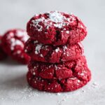 A stack of four vibrant red velvet cake mix cookies dusted generously with white powdered sugar.
