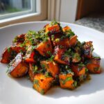 Close-up of roasted sweet potato cubes tossed in a vibrant green herb dressing, perfect for sweet potato salad.