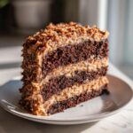 A tall slice of moist german chocolate cake recipe showing three layers of dark chocolate cake and coconut-pecan frosting.