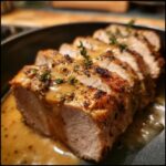 Close-up of perfectly cooked and sliced pork loin roast drizzled with herb gravy and thyme sprigs.