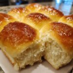 A close-up of freshly baked, soft Homemade dinner rolls with a shiny, golden-brown butter glaze, one roll pulled apart.