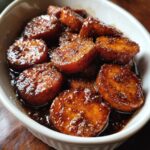 Close-up of thick-cut southern candied yams coated in a rich, dark, glossy brown sugar glaze, served in a white bowl.